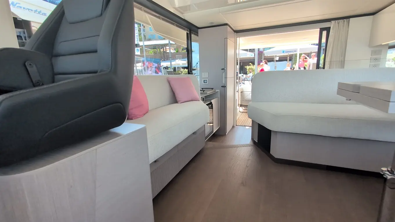 Modern yacht interior featuring a black helm seat, light grey couches with pink cushions, and a stylish wooden floor.